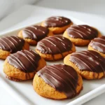 Für diese köstlichen Kekse brauchst du: - 1 Tasse Kürbispüree - 1 Tasse brauner Zucker - 1/2 Tasse weißer Zucker - 1/2 Tasse ungesalzene Butter, weich - 1 großes Ei - 1 Teelöffel Vanilleextrakt - 2 Tassen Weizenmehl - 1 Teelöffel Natron - 1 Teelöffel Backpulver - 1 Teelöffel gemahlener Zimt - 1/2 Teelöffel gemahlene Muskatnuss - 1/2 Teelöffel gemahlener Ingwer - 1/4 Teelöffel Salz - 1 Tasse Zartbitterschokoladenstückchen - 1 Esslöffel Kokosöl oder Pflanzenöl Diese Zutaten sind wichtig. Sie geben den Keksen ihren tollen Geschmack und die weiche Konsistenz. Kürbispüree sorgt für Feuchtigkeit und Geschmack. Zimt und Muskatnuss bringen Wärme, ideal für den Herbst. Für die Dekoration der Kekse kannst du verwenden: - Übrig gebliebene geschmolzene Schokolade - Meersalz für den besonderen Kick Die zusätzliche Schokolade macht die Kekse noch leckerer. Ein Hauch von Meersalz gibt einen tollen Kontrast zum süßen Geschmack. Achte beim Einkaufen auf hochwertige Zutaten: - Kürbispüree: Kaufe reines Püree ohne Zusätze. - Zucker: Brauner Zucker sollte feucht und klumpig sein. - Schokolade: Wähle Zartbitterschokolade mit mindestens 60% Kakaoanteil. Hochwertige Zutaten machen einen großen Unterschied. Sie sorgen dafür, dass deine Kekse nicht nur gut schmecken, sondern auch gut aussehen. Heize deinen Ofen auf 175 °C vor. Das ist wichtig, damit die Kekse gleichmäßig backen. Lege ein Backblech mit Backpapier aus. So kleben die Kekse nicht fest. Nimm eine große Schüssel. Gib das Kürbispüree, den braunen Zucker und den weißen Zucker hinein. Mische die Zutaten gut, bis sie eine glatte Masse bilden. Das Kürbispüree gibt den Keksen Feuchtigkeit und Geschmack. In einer separaten Schüssel vermenge das Mehl, Natron, Backpulver, Zimt, Muskatnuss, Ingwer und Salz. Rühre die trockenen Zutaten gut durch. Dann füge sie langsam zur Kürbismischung hinzu. Rühre nur, bis alles gerade vermischt ist. Übermixen macht die Kekse hart. Nutze einen Esslöffel oder Keksteiler, um Portionen Teig auf das Backblech zu setzen. Lass genug Platz zwischen den Keksen, da sie beim Backen auseinanderlaufen. Backe die Kekse 12-15 Minuten. Sie sollten leicht gebräunt und fest sein. Lass sie fünf Minuten auf dem Blech abkühlen, bevor du sie auf ein Gitter legst. Während die Kekse abkühlen, schmelze die Zartbitterschokoladenstückchen mit dem Kokosöl in der Mikrowelle. Erhitze die Mischung in 30-Sekunden-Intervallen und rühre zwischendurch. Sobald die Schokolade glatt ist, tauche die Oberseite der Kekse hinein. Lass die überschüssige Schokolade abtropfen. Lege die getauchten Kekse wieder auf das Backpapier. Lass die Schokolade bei Raumtemperatur fest werden. Du kannst die Kekse auch kurz in den Kühlschrank stellen, um den Vorgang zu beschleunigen. Serviere die Kekse auf einem schönen Teller, vielleicht mit etwas geschmolzener Schokolade darüber. Ein Hauch von Meersalz bringt einen tollen Kontrast. Um die besten Kekse zu backen, heize deinen Ofen auf 175 °C vor. Das sorgt für eine gleichmäßige Hitze. Backe die Kekse für 12 bis 15 Minuten. Sie sollten leicht gebräunt sein. Achte darauf, dass sie fest, aber nicht hart sind. Wenn du sie zu lange backst, werden sie trocken. Ein häufiger Fehler ist, den Teig zu lange zu mischen. Mische nur so lange, bis alles gut vermengt ist. Ein anderer Fehler ist, die Kekse zu nah beieinander zu setzen. Lass genug Platz zwischen ihnen, damit sie beim Backen auseinanderlaufen können. Wenn du das Kürbispüree selbst machst, achte darauf, dass es gut abgetropft ist. Zu viel Flüssigkeit kann die Konsistenz der Kekse beeinträchtigen. Um die Kekse schön zu präsentieren, serviere sie auf einem dekorativen Teller. Du kannst die übrig gebliebene geschmolzene Schokolade kunstvoll über die Kekse träufeln. Ein Hauch von Meersalz über der Schokolade gibt einen tollen Kontrast. Du kannst auch Nüsse oder Streusel hinzufügen. So wirken die Kekse noch ansprechender. {{image_4}} Um diese Kekse glutenfrei zu machen, tauschen Sie das Weizenmehl aus. Verwenden Sie stattdessen eine Mischung aus glutenfreiem Mehl. Achten Sie darauf, dass Ihre anderen Zutaten ebenfalls glutenfrei sind. Diese Anpassung macht die Kekse für alle zugänglich. Sie schmecken immer noch lecker. Die Schokolade ist der Star dieser Kekse. Aber Sie können variieren! Verwenden Sie Vollmilchschokolade oder weiße Schokolade. Dunkle Schokolade hat einen starken Geschmack. Weiße Schokolade bringt Süße. Beide Optionen schmecken toll. Experimentieren Sie mit verschiedenen Schokoladensorten, um Ihren Favoriten zu finden. Fügen Sie Nüsse oder getrocknete Cranberries hinzu, um den Keksen mehr Textur und Geschmack zu geben. Walnüsse oder Pekannüsse passen gut. Cranberries bringen eine fruchtige Note. Mischen Sie diese Zutaten einfach unter den Teig. Sie machen die Kekse noch interessanter und leckerer! Um frisch gebackene Kekse richtig zu lagern, lege sie in einen luftdichten Behälter. Ich empfehle, sie bei Raumtemperatur zu lagern. So bleiben sie weich und lecker. Wenn du die Kekse in den Kühlschrank legst, werden sie hart. Wenn du sie länger aufbewahren möchtest, kannst du sie auch einfrieren. Um die Kekse einzufrieren, lasse sie zuerst ganz abkühlen. Lege sie dann in einen geeigneten Gefrierbehälter. Ich rate dir, die Kekse mit Backpapier zwischen den Schichten zu trennen. So kleben sie nicht zusammen. Du kannst die Kekse bis zu drei Monate im Gefrierfach lagern. Zum Auftauen lege sie einfach bei Zimmertemperatur auf einen Teller. Die Haltbarkeit der Schokoladengetauchten Kürbiskekse beträgt bei richtiger Lagerung etwa eine Woche. Wenn du sie kühl und trocken hältst, bleiben sie frisch. Achte darauf, dass du keine feuchten Hände verwendest, wenn du die Kekse anfasst. Das kann ihre Haltbarkeit beeinträchtigen. Die Schokoladengetauchten Kürbiskekse halten sich bis zu einer Woche. Bewahren Sie sie in einem luftdichten Behälter auf. So bleiben sie frisch und lecker. Wenn Sie sie länger aufbewahren möchten, können Sie sie einfrieren. In einem Gefrierbeutel halten sie bis zu drei Monate. Ja, Sie können Kürbispüree leicht selbst machen. Nehmen Sie einen kleinen Kürbis, schneiden Sie ihn auf und entfernen Sie die Kerne. Backen Sie die Hälften bei 180 °C für etwa 45 Minuten. Dann löffeln Sie das Fruchtfleisch heraus und pürieren es glatt. Selbstgemachtes Kürbispüree schmeckt frisch und intensiv. Kekse können auseinanderlaufen, wenn der Teig zu heiß ist oder nicht genug gekühlt wurde. Achten Sie darauf, dass die Butter weich, aber nicht geschmolzen ist. Formieren Sie die Kekse und stellen Sie sie für 15 Minuten in den Kühlschrank. So bleiben sie in Form und laufen nicht auseinander. Für das Dippen empfehle ich Zartbitterschokolade. Sie hat einen tollen Geschmack und passt gut zu Kürbis. Sie können auch Milchschokolade oder weiße Schokolade verwenden, je nach Vorliebe. Achten Sie darauf, eine hochwertige Schokolade zu wählen, um das beste Ergebnis zu erzielen. Zusammenfassend haben wir die Hauptzutaten für schokoladengetauchte Kürbiskekse und wichtige Tipps besprochen. Ich erklärte die Schritt-für-Schritt-Anleitung zum Backen und Dekorieren. Außerdem bieten die Variationen für jeden Geschmack etwas. Richtige Lagerung sichert die Frische. Denken Sie daran, das Kürbispüree selbst zu machen, um den besten Geschmack zu erzielen. Diese Kekse sind einfach lecker und ein toller Snack für jede Gelegenheit. Bereiten Sie Ihre eigenen zu und genießen Sie die Freude des Backens!